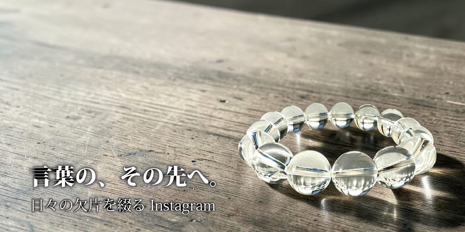 木目調のテーブルに水晶のブレスレットが置かれた静謐なバナー。左下に『言葉の、その先へ。日々の欠片を綴る Instagram』の文字。