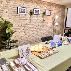 「天智開道」芝大門A鑑定会の会場。温かみのあるベージュのレンガ調の壁に、植物の額縁や観葉植物の緑が美しく映える、お洒落なアトリエのような雰囲気の部屋です。
優しいグリーンのクロスが敷かれた大きなテーブルの上には、暖色に灯る球体照明や鑑定のための様々なツールが丁寧に並べられ、奥ではスタンドライトが空間を柔らかく照らしています。
どこかホッとするような温もりと、深い対話への期待感が同居しており、緊張した心を優しく包み込んで、自分の未来へ前向きに向き合える鑑定会場です。