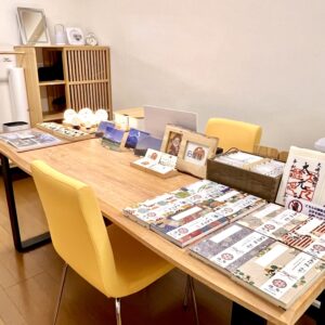 「天智開道」仙台A鑑定会の会場。温かみのある木目の大きなテーブルに、パステルイエローの優しい色合いの椅子が並ぶ、ナチュラルで明るい雰囲気の部屋です。
テーブルの上にはたくさんの書籍や案内が整然と並べられ、奥の棚の上には柔らかな光を放つ球体の間接照明やインテリアが品良く飾られています。
ほっと心が和むような家庭的な温もりと清潔感に包まれており、初めての方でも緊張することなく、リラックスしたリラックスした気分で気軽に相談ができる鑑定会場です。