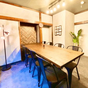 「天智開道」北千住A鑑定会の会場。古民家風の太い木柱の梁と白壁に囲まれた、落ち着きのある和モダンな雰囲気の部屋です。
中央には重厚な木製の長テーブルとシックな黒い鉄製の椅子が並び、天井からは温かい電球色のライトが空間を優しく照らしています。
大人の隠れ家のような静けさと、包み込まれるような深い安心感があり、周囲の雑音を忘れて自分の人生の根源とじっくり向き合える、特別な熱量を持った鑑定会場です。