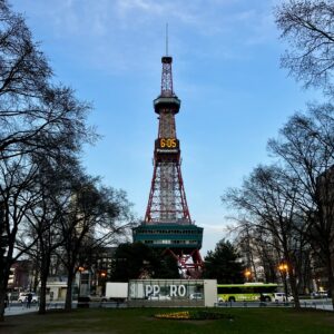 夕暮れ時、大通公園にそびえ立つ「さっぽろテレビ塔」。電光掲示板に18:05の時刻が灯る風景。