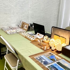 鑑定会の会場風景。若草色のクロスが敷かれたテーブルの上に、整然と並べられた石や御朱印帳。暖色のランプが灯り、訪れる人を優しく包み込む空間。