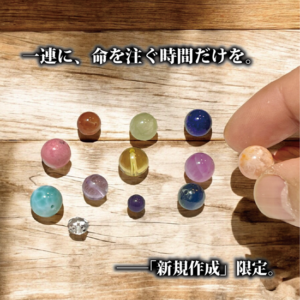 店主の指先が、オレンジ色の透過性が高い石を一粒、慎重に選び取っている瞬間。職人の静かな緊張感と、石に対する深い敬意が伝わる接写。
