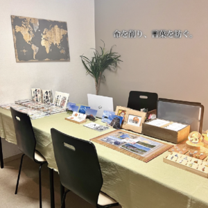 鑑定会の温かな空間。淡いグリーンのクロスに天然石や店主の作品が並び、傍らの観葉植物が生命力を添えている。「命を削り、言葉を紡ぐ。」という真摯な決意が宿る、安心感に満ちた場所。