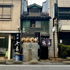 富山ブラックラーメンの元祖「西町大喜」の店舗外観。年季の入った渋い木造二階建ての建物に、「元祖富山ブラック」「西町大喜」と書かれた黒い大きな暖簾や上り旗が掲げられ、歴史と風格を感じさせる佇まい。