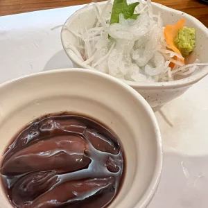 富山の居酒屋で出された、艶やかに光るホタルイカの沖漬けが盛られた小鉢と、その奥にある透き通った美しい白えびの刺身。大根のツマと大葉、ワサビが添えられている。
