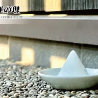 石屋蓮本店「瑞照庵」の玄関先。玉砂利が敷き詰められた足元に、白い小皿に美しく円錐状に盛られた盛り塩が置かれており、背景の壁には柔らかな日差しが差し込んでいます。左上には「開運の理 〜運を拓く、日々の暮らしの理〜」という文字が配置されています。