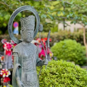 豊かな緑を背景に、柔らかな光を全身に浴びて佇む青銅の仏像。その表情は迷いを優しく受け止めるような、穏やかで慈愛に満ちた眼差し。