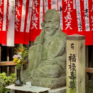 石造りの福禄寿尊。長い年月を経て苔むした表情は穏やかで、傍らに添えられた小さな花瓶の花からは、参拝者が静かに祈りを捧げ、その対話を大切に紡いできた日々の積み重ねが感じられる。