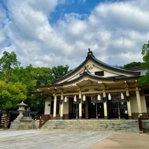 白壁と濃い色の木組み、そして気品のある和風の屋根が組み合わさった湊川神社の御本殿の正面像。朝の穏やかな光が境内全体を優しく包み込み、訪れる者の心を静かに鎮めるような清らかな聖域の佇まい。