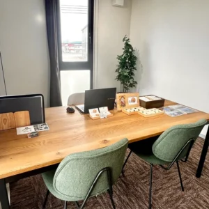山形鑑定会の会場内の様子。温かみのある大きな木目のデスクが中央に置かれ、ノートパソコンやショップカードが整然と並べられています。緑色の心地よい椅子が用意されており、大きな窓から差し込む光が穏やかな空間を演出しています。初めての方も緊張せず、ゆっくりと向き合える落ち着いた雰囲気です。